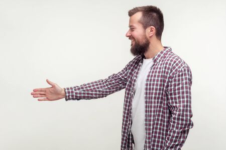 Side view of friendly bearded man in casual plaid shirt reaching out hand to handshake, getting acquainted at job interview, meeting new people. indoor studio shot isolated on white backgroundの写真素材