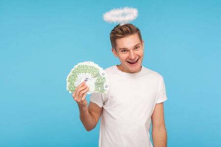 Portrait of joyful happy man in casual white t-shirt and with halo over head holding fan of euro...