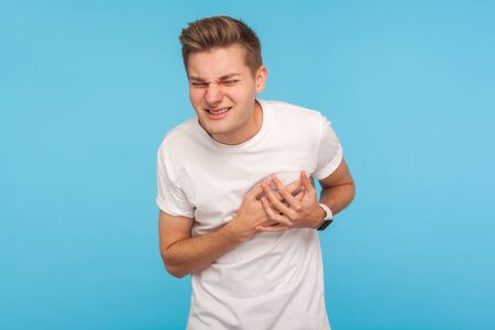 Heart attack. Unhealthy overworked man in white t-shirt clutching chest, needs emergency of acute...