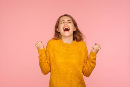 Portrait of delighted joyful ginger girl in sweater standing with head up and raised arms, closed...