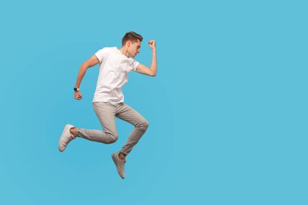 Full length, motivated man in white t-shirt and casual pants running in air with serious confident...