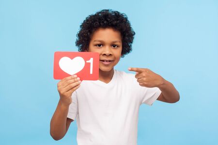 Cute lovely young boy with curly hair pointing to heart Like symbol, icon to appreciate content,...