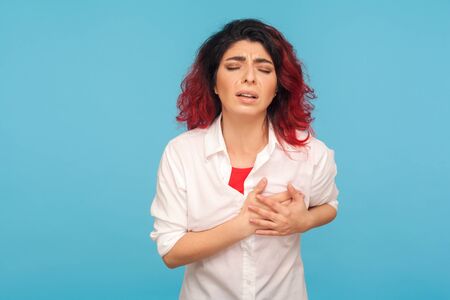 Portrait of ill woman with red hair suffering chest pain, holding sore place with painful expression, risk of breast cancer, healthcare and medical concept. studio shot isolated on blue backgroundの写真素材