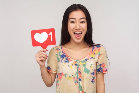 Delighted enthusiastic girl in blouse showing internet heart icon, recommending to subscribe and...
