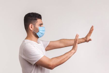 Side view of alarming man in hygienic protective mask gesturing stop, afraid of coronavirus...