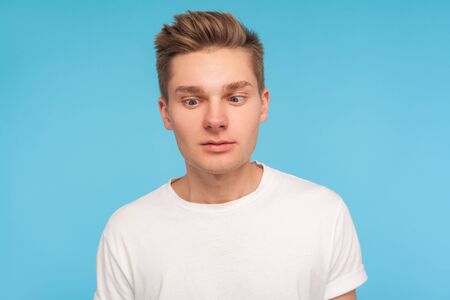 Portrait of funny comic young man in casual white t-shirt looking cross-eyed with awkward silly dumb...