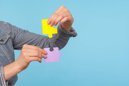 Closeup of female hands holding colorful pieces of puzzle, two jigsaw parts of one, symbol of...