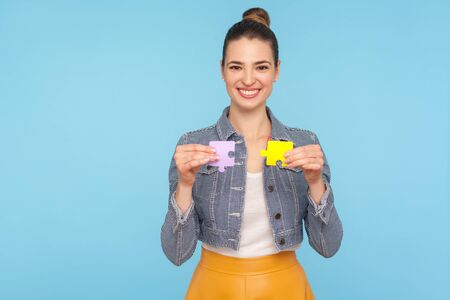 Fascinating joyful fashionably dressed woman with hair bun holding colorful pieces of puzzle, two...