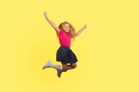 Full length portrait of beautiful little girl with long blond hair in dress jumping in air, inspired child flying and celebrating carefree life. indoor studio shot isolated on yellow backgroundの写真素材