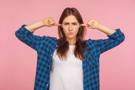 Don't want to listen! Portrait of displeased upset girl in checkered shirt closing ears and looking...