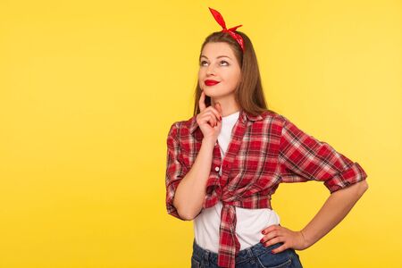 Portrait of pensive attractive pinup girl in checkered shirt and headband standing thoughtful,...