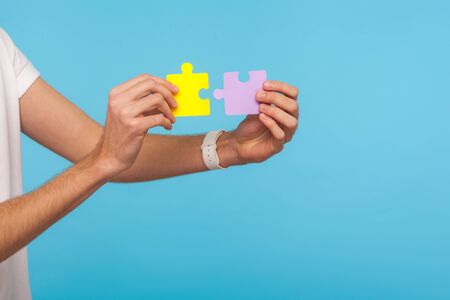 Closeup of male hands holding two puzzle parts, ready to connect colorful jigsaw pieces, symbol of...