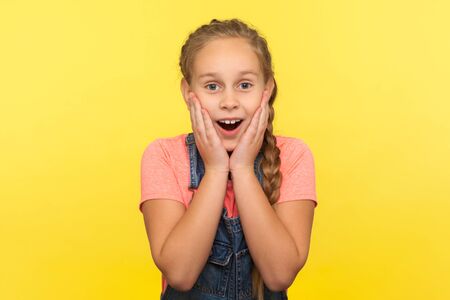 Awesome unexpected event. Portrait of astonished little girl touching face in surprise, expressing...