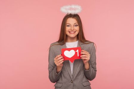 Portrait of adorable brunette woman with nimbus in business suit holding network heart Like icon and...