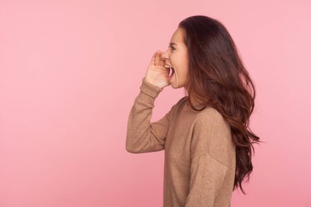 Attention, important message! Side view of young woman with brunette wavy hair shouting news or...