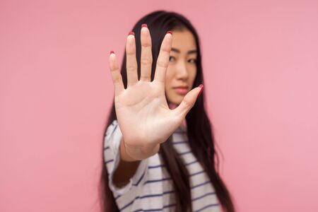 Ban, prohibition concept. Portrait of serious girl with brunette hair holding out hand, showing Stop, block gesture, warning of danger, refusing to communicate. studio shot isolated on pink backgroundの写真素材