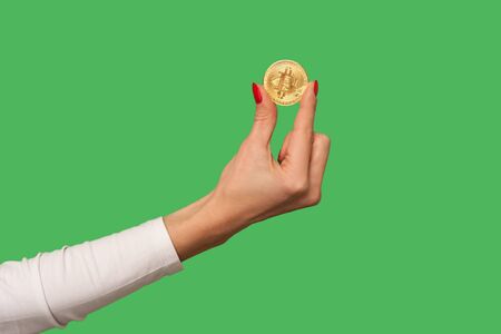 Closeup of woman hand holding golden bitcoin, advertise of digital money btc coin for e-commerce, blockchain technology and cryptocurrency, electronic investment. indoor studio shot, green backgroundの写真素材