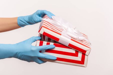Profile side view closeup of human hand in blue surgical gloves holding and opening red white striped gift box. indoor, studio shot, isolated on gray background.の写真素材