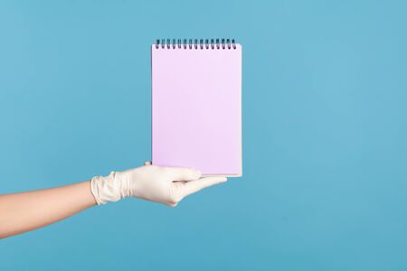 Profile side view closeup of human hand in white surgical gloves holding purple notepad in hand and...