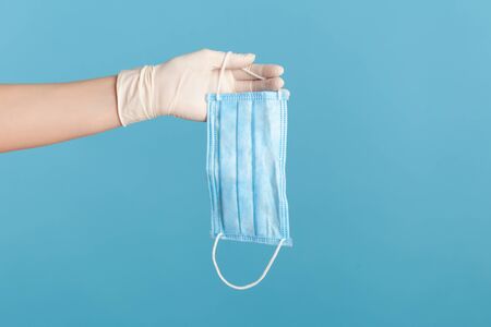 Profile side view closeup of human hand in white surgical gloves holding blue surgical medical mask....