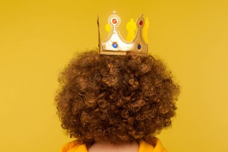 Closeup of head with golden crown on curly afro hairdo, concept of superior privileged status, big ambitions and dreams to become leader in charge. indoor studio shot isolated on yellow backgroundの写真素材