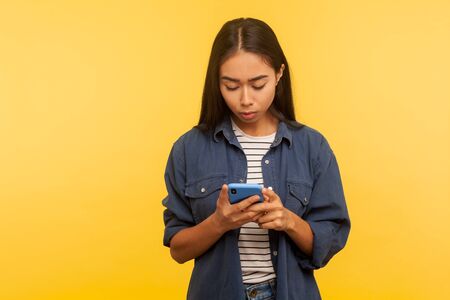 Portrait of attentive serious girl in stylish denim shirt typing message, dialing number calling on...