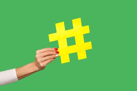 Closeup of woman hand holding big yellow hashtag sign, tagging famous internet post, sharing viral content, popular idea. studio shot isolated on green backgroundの写真素材