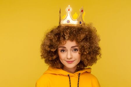 I am queen! Closeup of lovely happy curly-haired woman wearing crown on head and smiling, concept of self confidence in success, self-motivation and dreams to be best. indoor studio shot, isolatedの写真素材