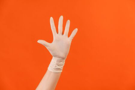 Profile side view closeup of human hand in white surgical gloves showing number five with hand or waving hand to greeting. indoor, studio shot, isolated on orange background.の写真素材