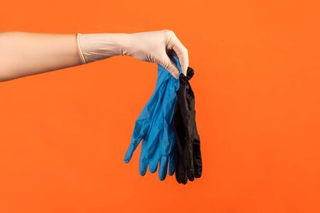 Profile side view closeup of human hand in white surgical gloves holding blue and black gloves....