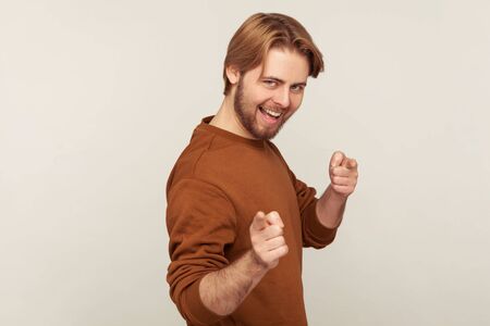 Hey there, we need you! Portrait of carefree cheerful man with beard wearing sweatshirt pointing...
