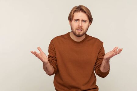 How could you? Portrait of irritated annoyed bearded man in sweatshirt standing with raised hands and indignant expression, asking reason of conflict. indoor studio shot isolated on gray backgroundの写真素材