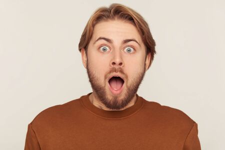 Closeup portrait of surprised bearded man screaming in sudden fright and shock, looking at camera with astonished expression, open mouth in amazement. indoor studio shot isolated on gray backgroundの写真素材