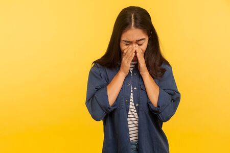 Portrait of upset dramatic girl in denim shirt crying with sorrow, wiping tears, feeling lonely hopeless, desperate emotions, worried about troubles. indoor studio shot isolated on yellow backgroundの写真素材