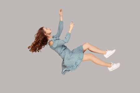Hovering in air. Relaxed beautiful girl ruffle dress and curly soaring hair levitating, flying in...