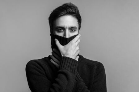 Portrait of stylish handsome young man in warm sweater, covering mouth with high collar and looking pensive thoughtful, male fashion, vogue concept. black and white, indoor studio shot isolatedの写真素材