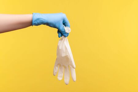Profile side view closeup of human hand in blue surgical gloves holding white gloves. indoor, studio...