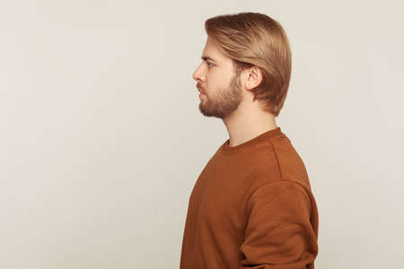 Profile of confident calm handsome man with neat hair and beard wearing sweatshirt standing, looking...