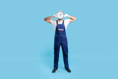 Full length expert worker man in uniform pointing at laptop with mock up blank display, showing empty place for advertise, message or repair service order. studio shot isolated on blue backgroundの写真素材