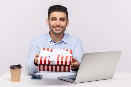 Happy businessman sitting in office workplace, pointing empty sheet and smiling at camera, showing...