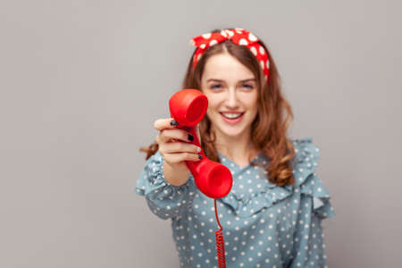 Take it, answer call! Charming happy pinup girl giving phone handset looking at camera, smiling looking friendly joyful, helpful contact center, customer support. studio shot isolated gray background,の写真素材