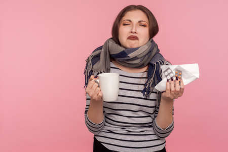Portrait of ill woman in scarf making miserable face and holding tea cup, crying looking...