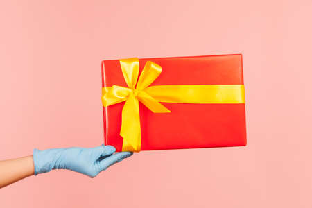 Profile side view closeup of human hand in blue surgical gloves holding red gift box. sharing,...
