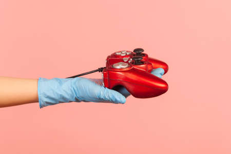 Profile side view closeup of human hand in blue surgical gloves holding red gamepad joystick....