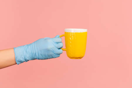 Profile side view closeup of human hand in blue surgical gloves holding and showing yellow cup of...