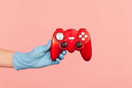 Profile side view closeup of human hand in blue surgical gloves holding red gamepad joystick....