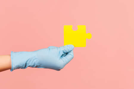 Profile side view closeup of human hand in blue surgical gloves holding one yellow puzzle piece....