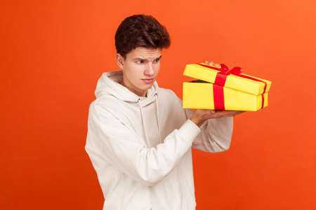 Profile portrait of doubtful teenager with fashionable hairdo in casual sweater looking inside gift...