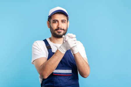 Optimistic worker in overalls and gloves keeping hands together in connection and agreement gesture. Profession of service industry, courier delivery, housekeeping maintenance. studio shot isolatedの写真素材
