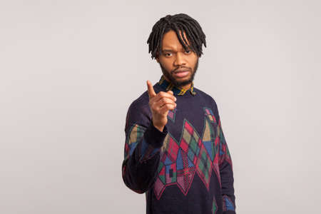 Strict serious african man with dreadlocks in casual sweatshirt pointing finger looking at camera,...